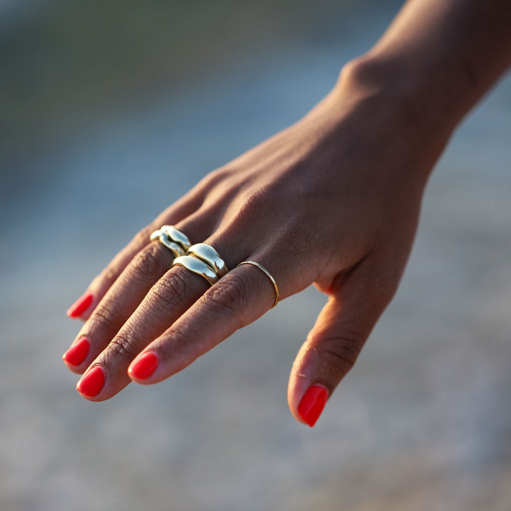 multiple chunky organically shaped gold rings on hand with bright red nails