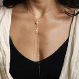 neck and chest with gold and pearl y shaped chain necklace against a dark background