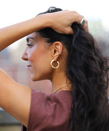 woman holding back her long dark hair wearing medium gold hoop earrings