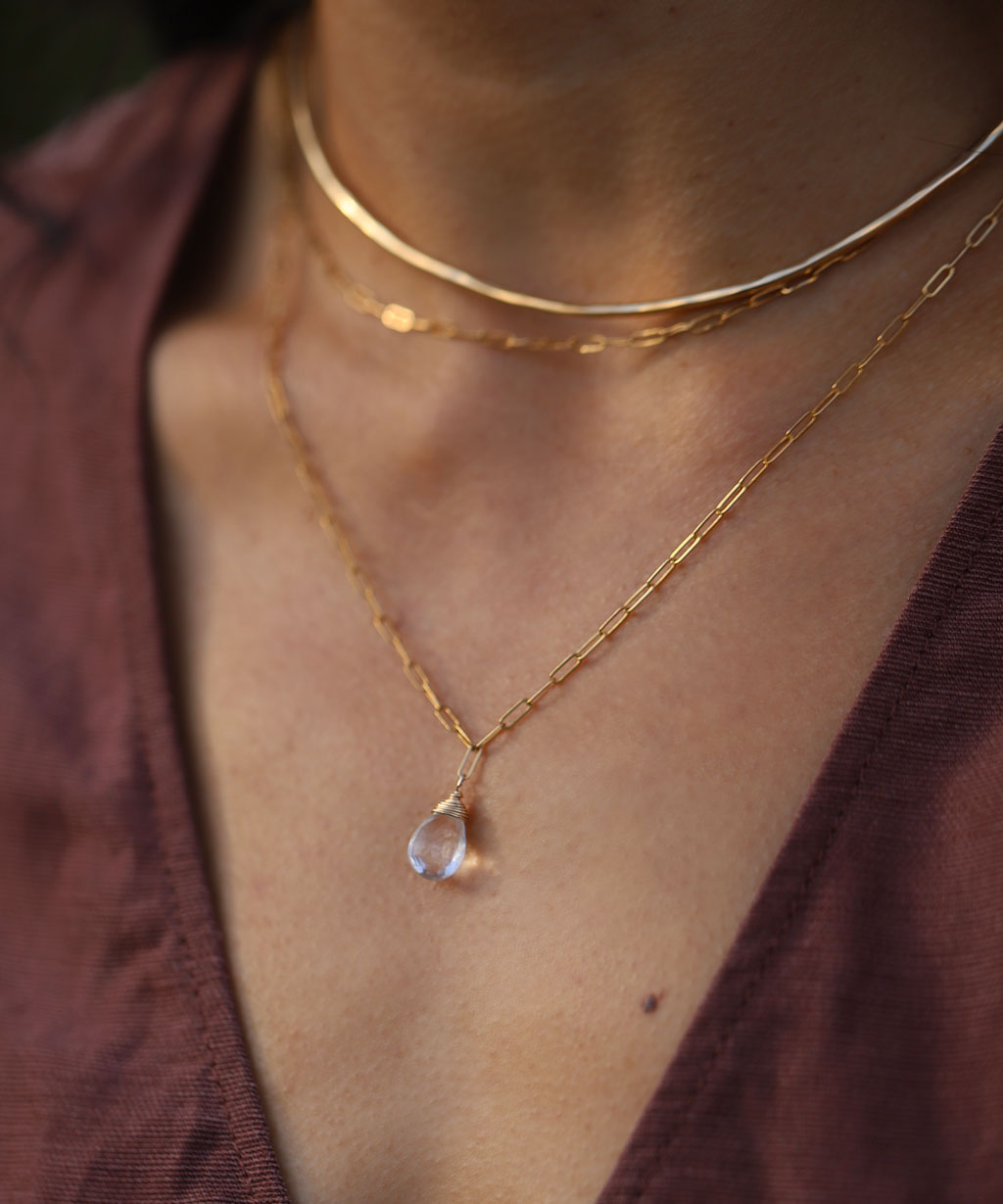 closeup of neck with delicate gold chain and quartz pendant necklace with gold wire choker