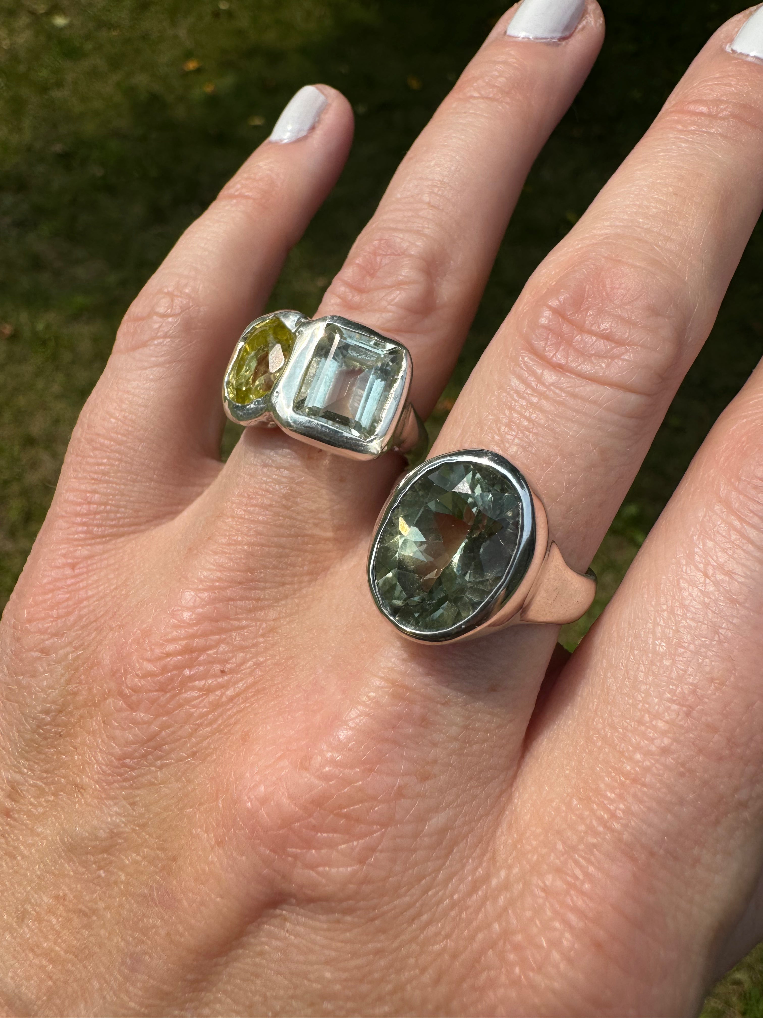 Hand wearing two rings with green gemstones against a natural background