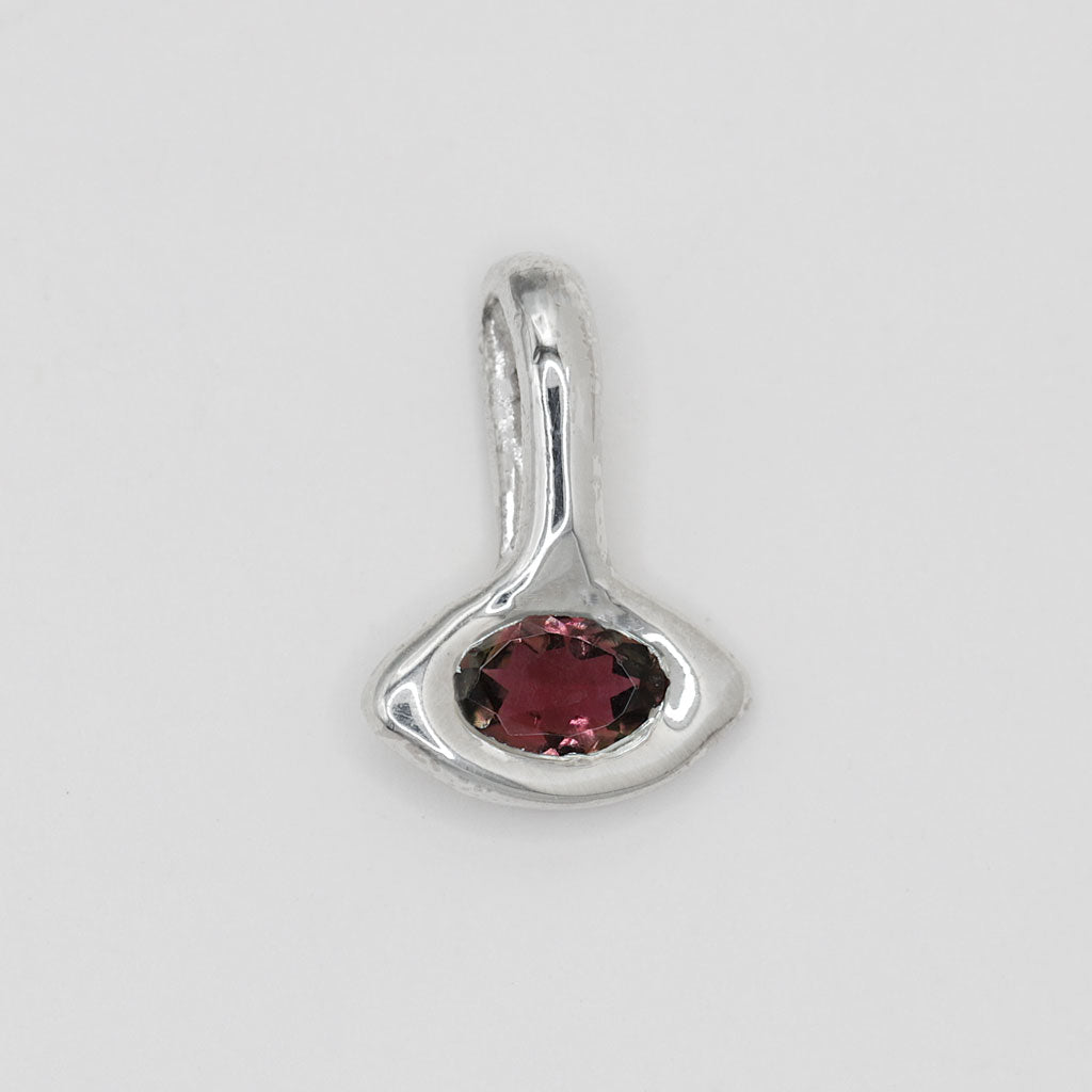 A sterling silver pendant featuring an organic, abstract teardrop-shaped setting with a faceted dark red gemstone in the center, shown on a plain light gray background.