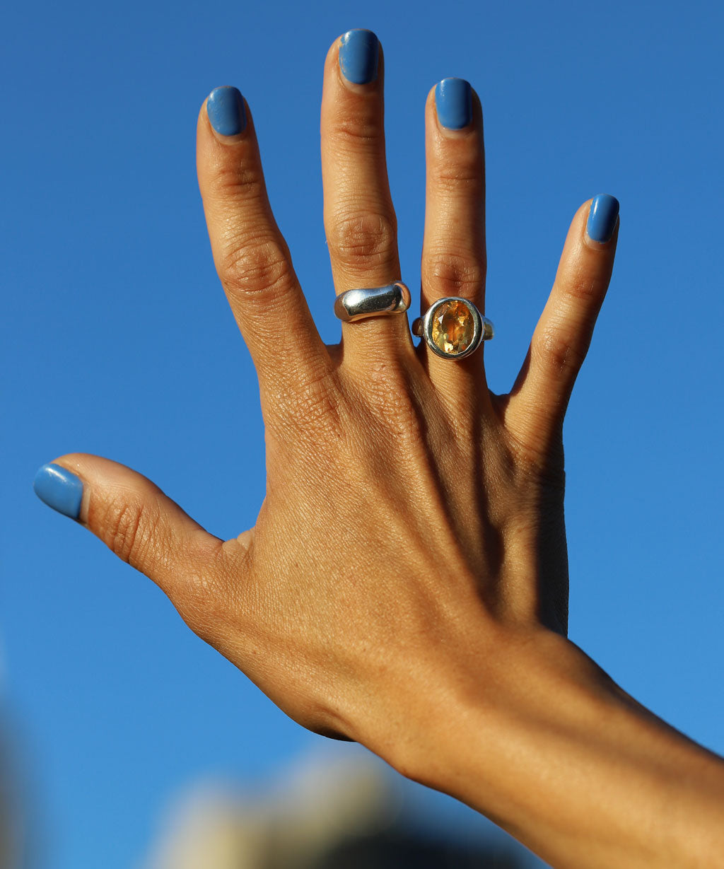 Hand with two silver and citrine rings against a blue sky