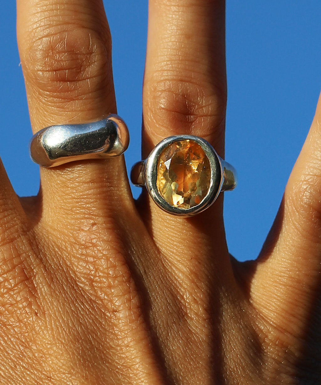 Hand wearing two silver and citrine rings with a blue background