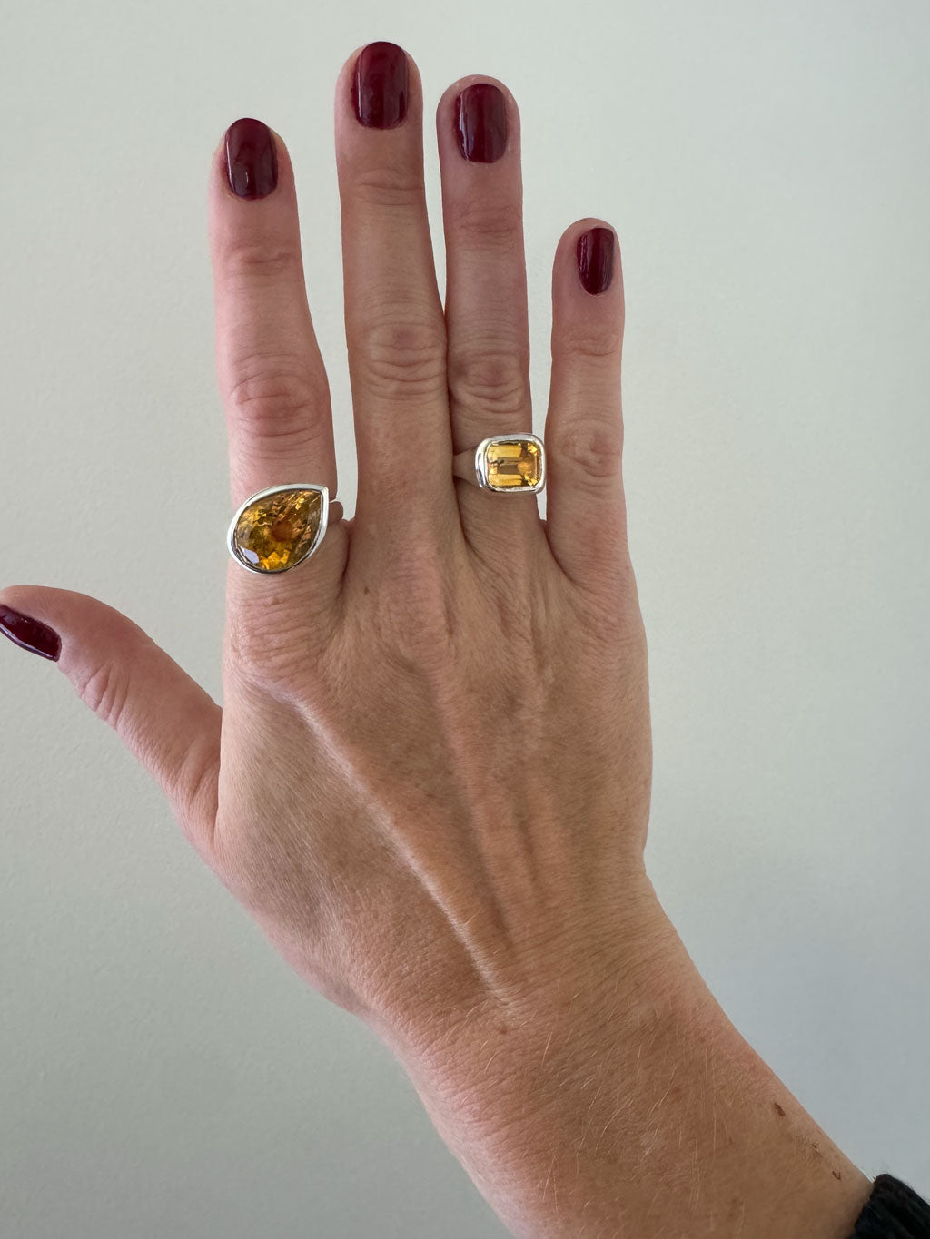 Hand wearing two rings with yellow gemstones on a plain background