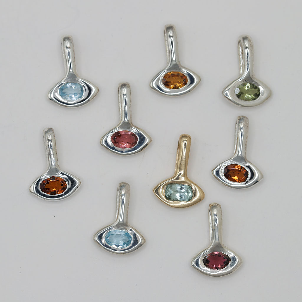 Nine small silver-toned pendant charms with curved settings and round gemstones in light blue, orange, green, and pink, arranged on a plain light background.