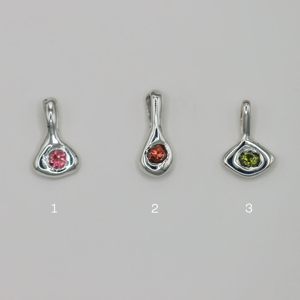 Three silver pendants with green and pink tourmaline gemstones on a gray background