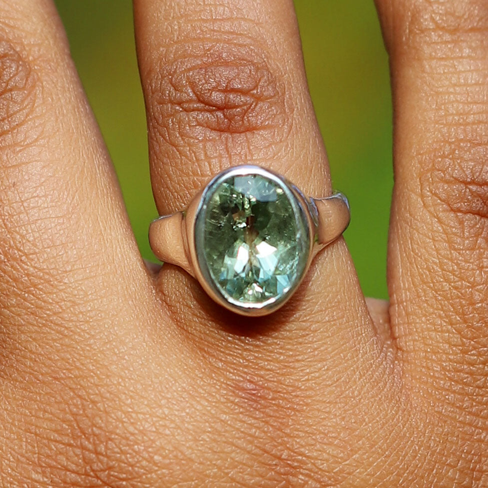 Ring with a green gemstone on a finger against a blurred green background