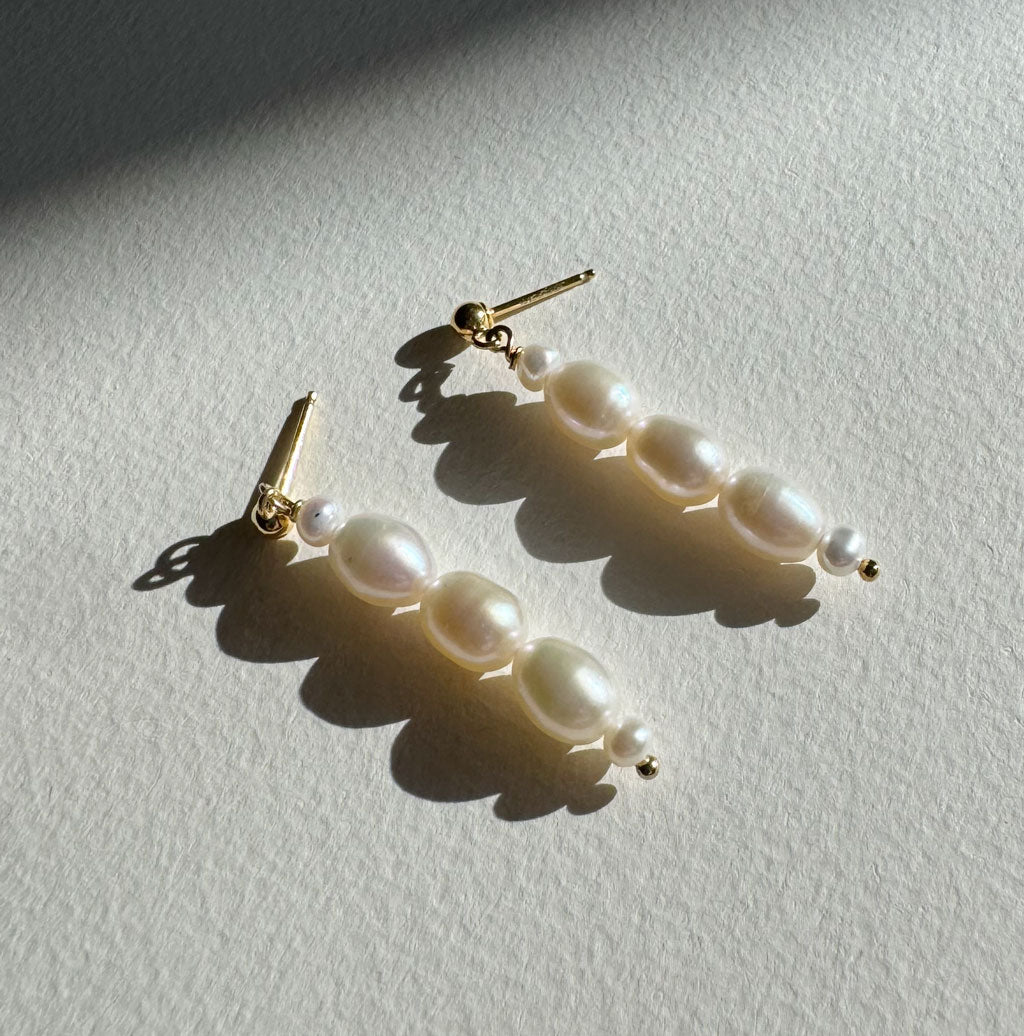 stilllife of long pearl drop earrings with gold studs