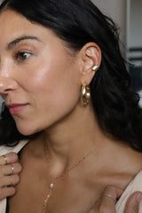 girl with black hair wearing gold hoop earrings and a pearl necklace