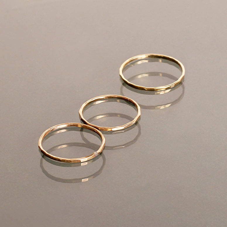three thin gold stacking rings on reflective surface