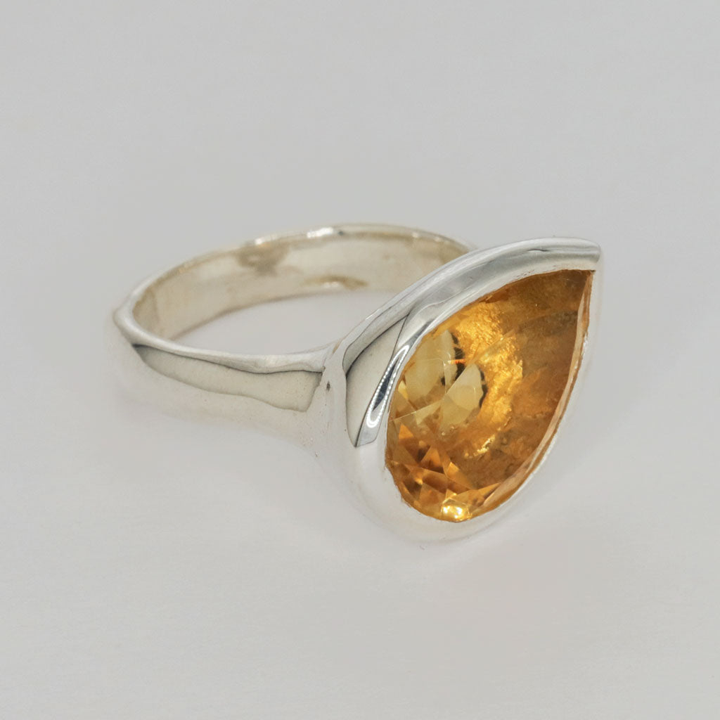 Silver ring with a large yellow citrine pear shaped gemstone on a light gray background