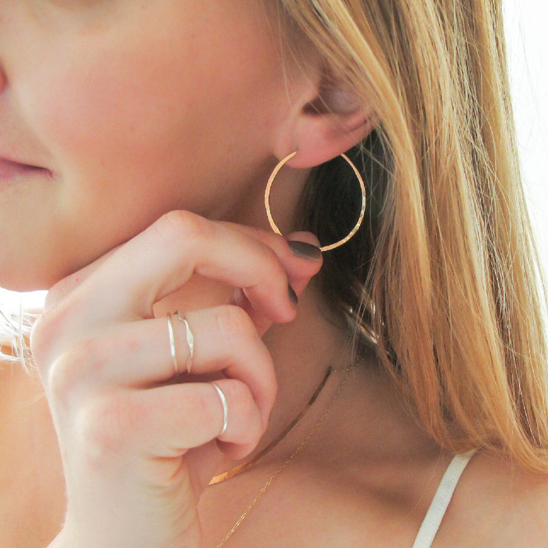 small gold endless hoop earrings on ear with fingers holding to show scale