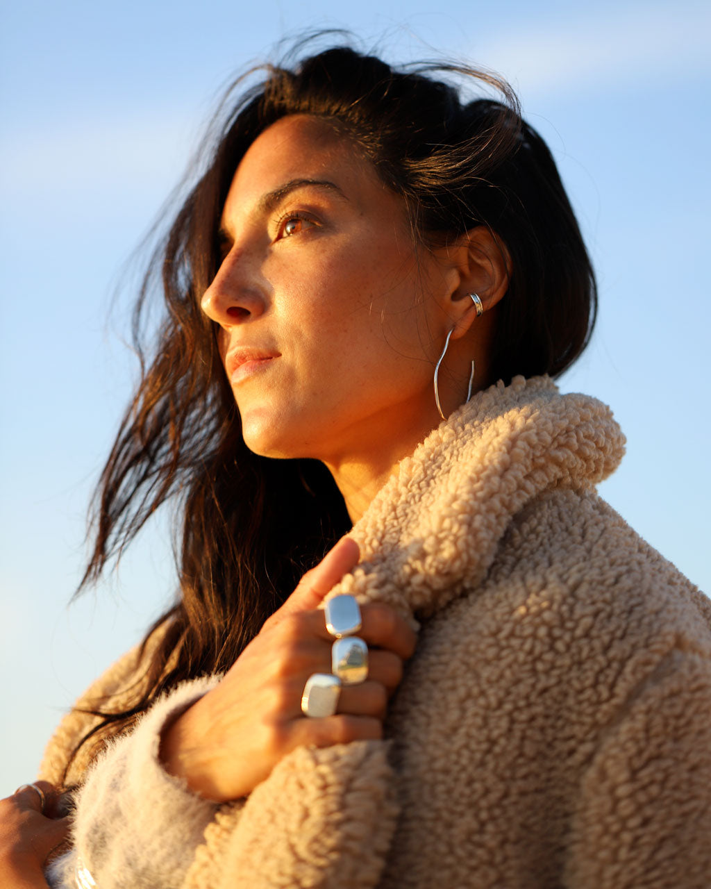 Brunette woman wearing Irregular silver hoops, hug hoop, big rings, and a wool jacket