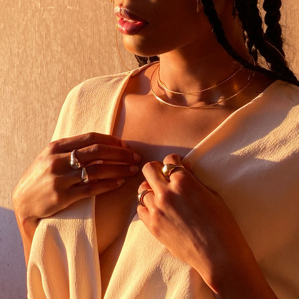 attractive black woman cleavage wearing curve ring on ring finger and globe ring on index finger against a wall facing sunset