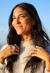 Brunette woman wearing big silver rings, hoops, and necklaces