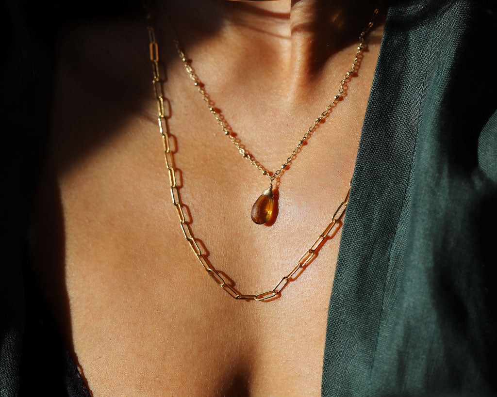 Woman wearing a gold link necklace, beaded pendant, and green shirt