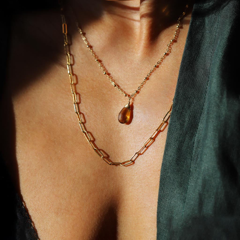 Woman wearing a gold link necklace, beaded pendant, and green shirt