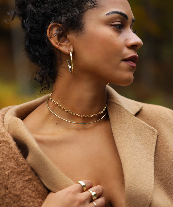 girl with dark curly hair in wool coat wearing gold choker necklaces and gold hoops
