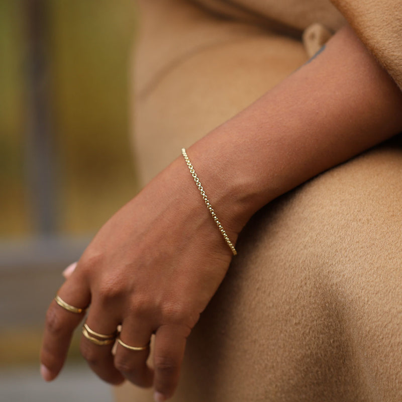 closeup of wrist with gold rolo chain resting against tan coat