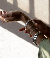 Woman wearing thick silver bracelets, silver link bracelets, big rings, and green shirt