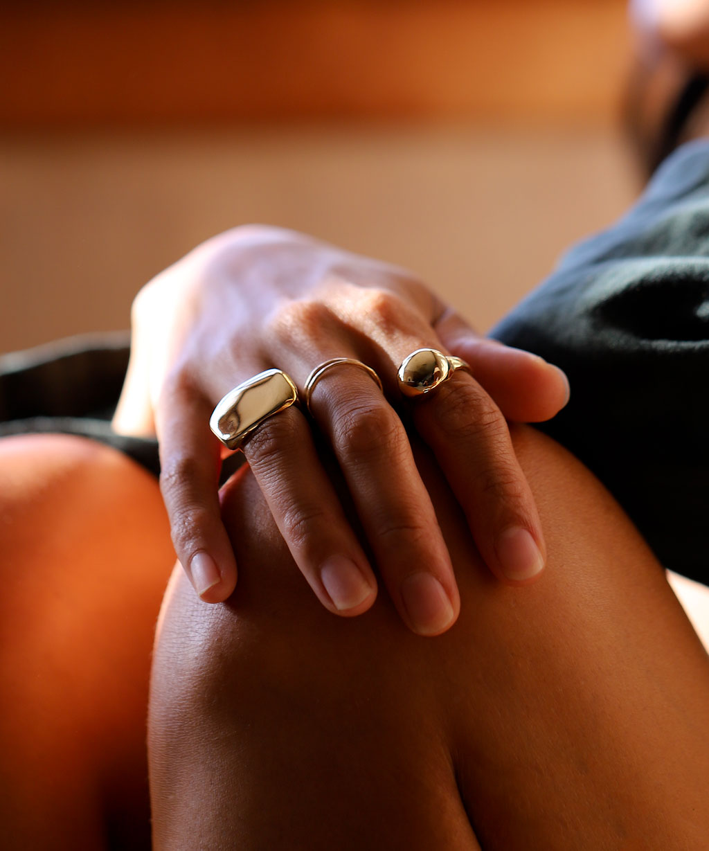 Womans hand on knee with gold plateau ring thin gold stacking rings and globe ring.