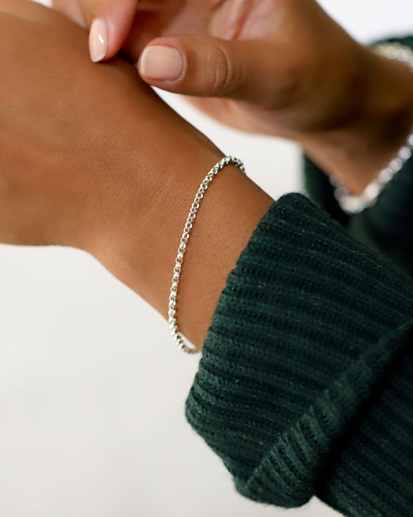 closeup of silver rolo chain bracelet on wrist with green sweater sleeve