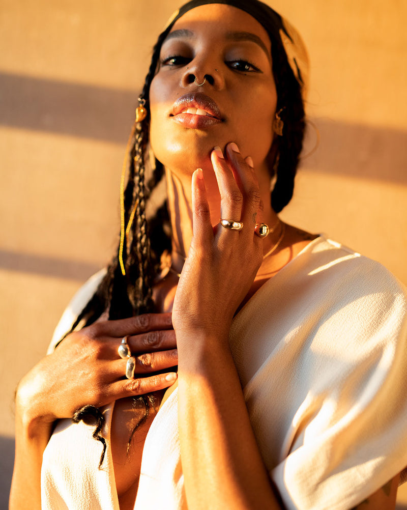 attractive black woman wearing curve ring on ring finger and globe ring on index finger against a wall facing sunset