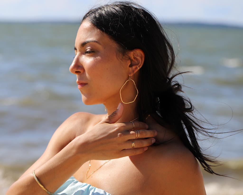brunette on a blue top at beach wearing 14k gold filled potatohead hoop earrings