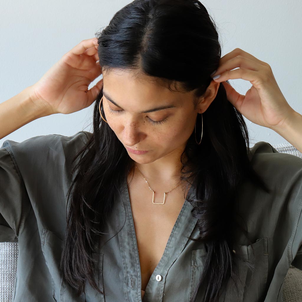 brunette on a grey shirt looking down wearing a 14k gold filled brick necklace