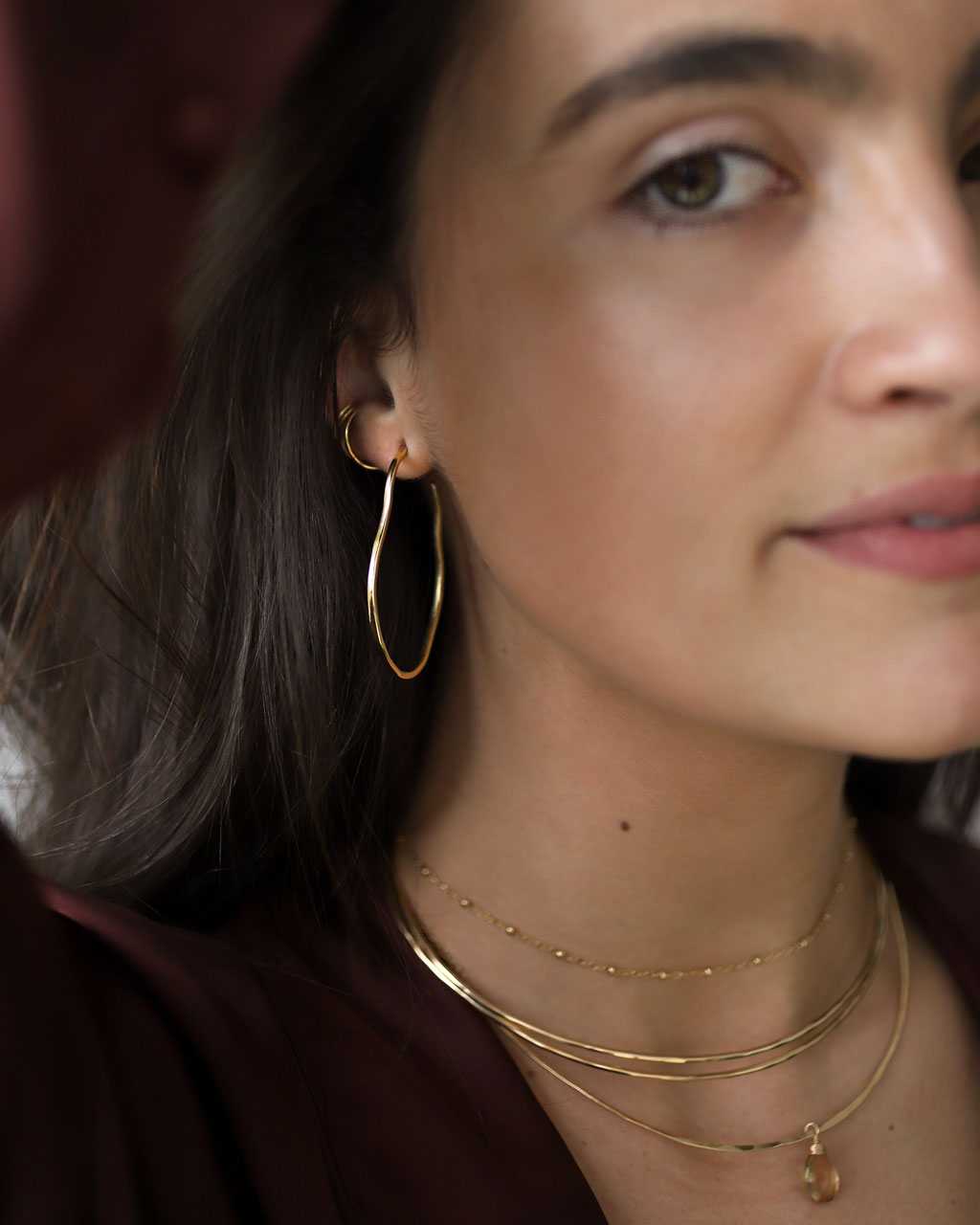brunette wearing brass maeve thin hoop earrings champagne quartz gemstonce arc necklace and two 14k gold filled halo collars
