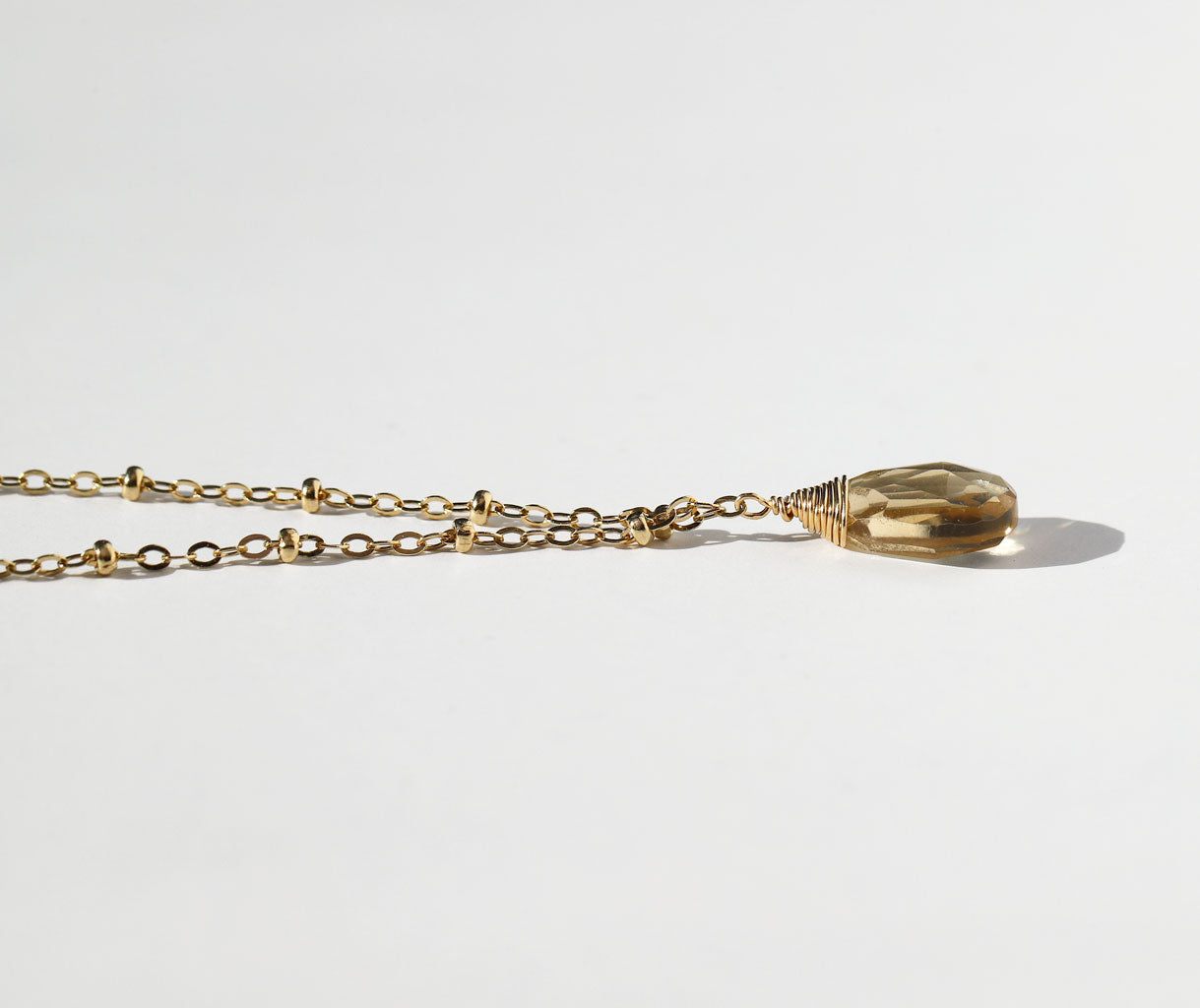 side shot of a 14k gold filled champagne quartz gemstone beaded pendant laying on a grey surface
