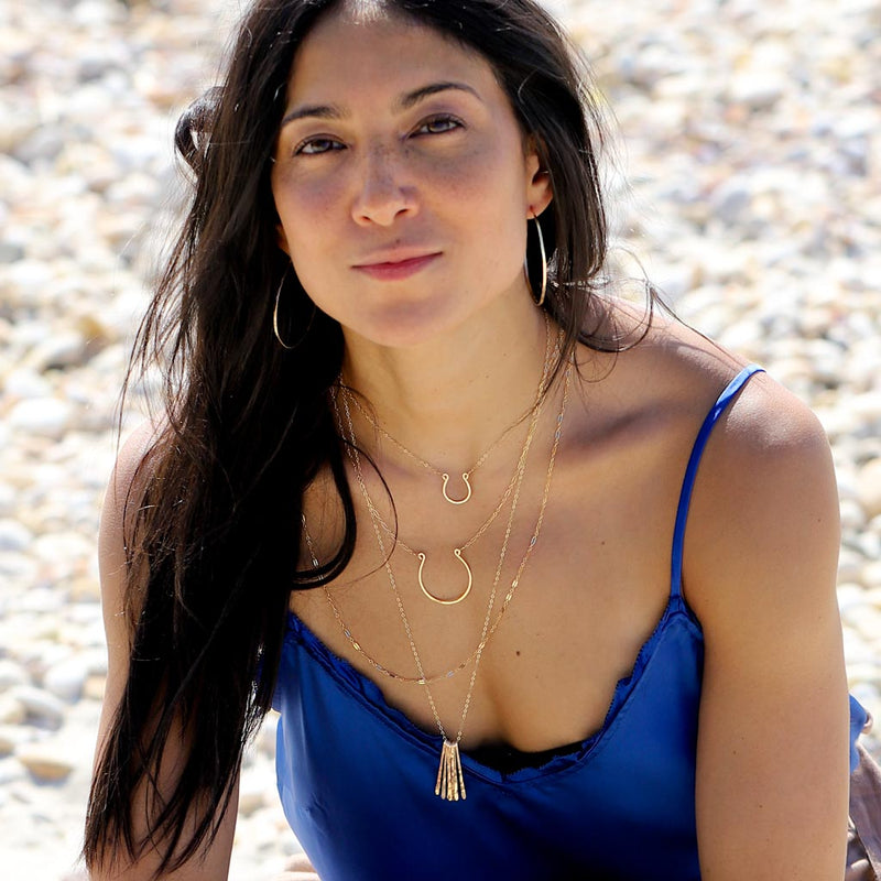 girl on beach with layered delicate gold horseshoe necklaces and gold hoop earrings