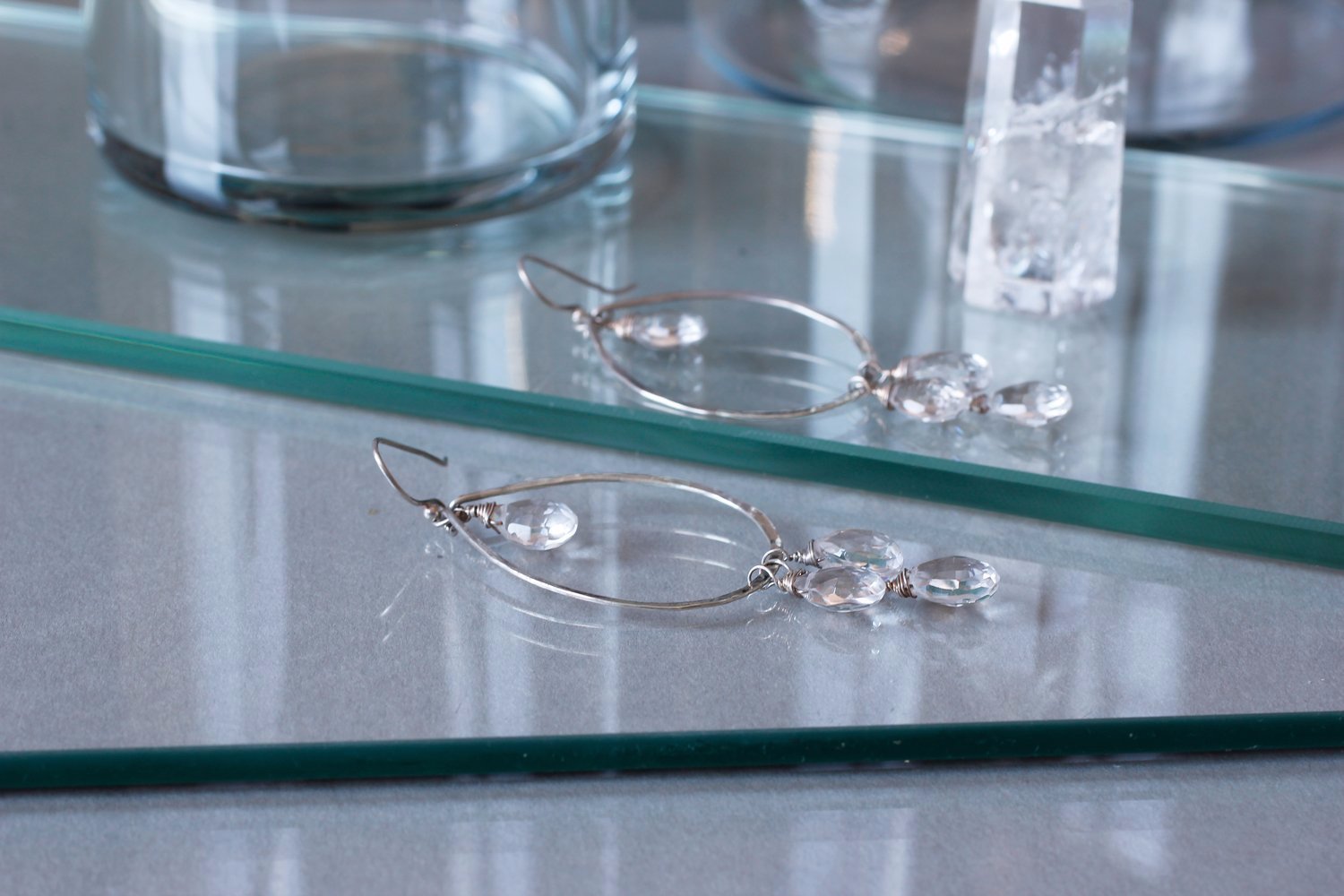 sterling silver crystal quartz dreamcatcher teardrop gemstone hoops laying on reflective glass surfaces
