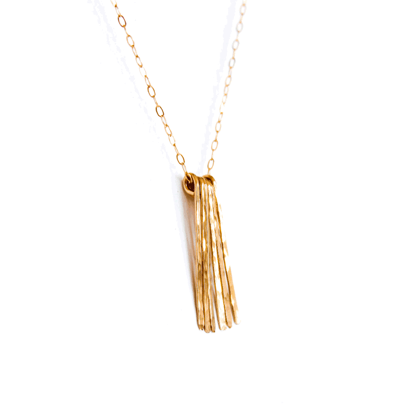 diagonal shot of a 14k gold filled different strokes fringe pendant necklace on a white surface