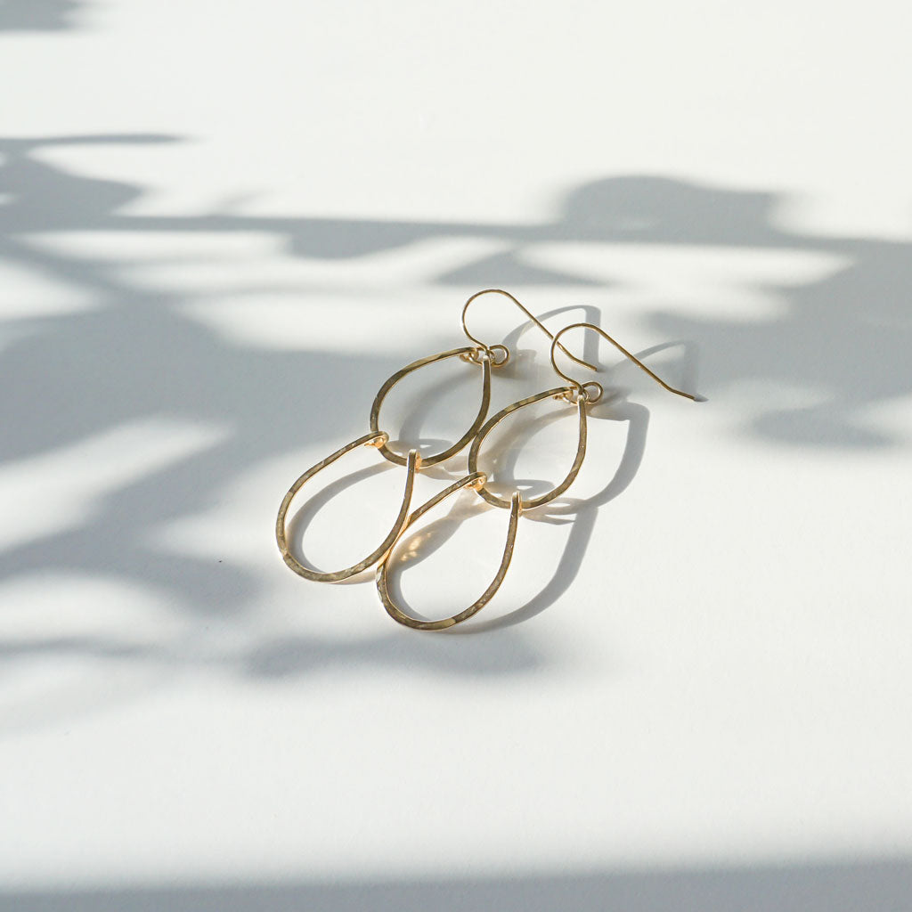 14k gold filled baby double drop earrings laying on a white surface partially under sunlight