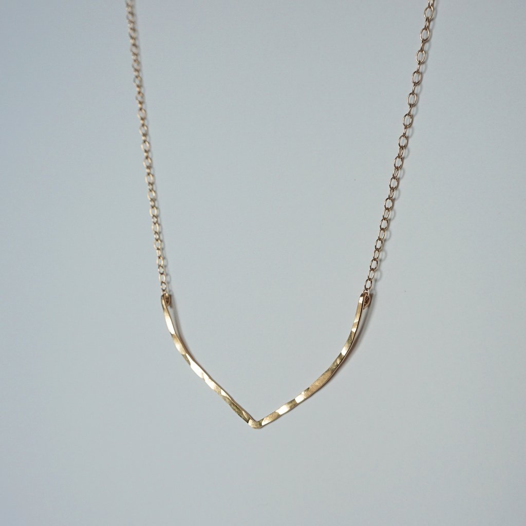 14k gold filled flight necklace on a grey surface partially reflecting light