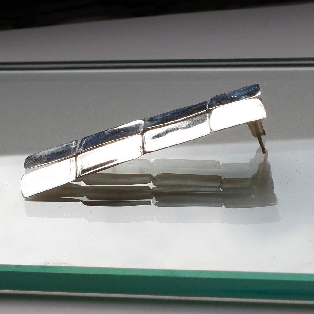 side shot of sterling silver four square post earrings laying on a glass surface under light