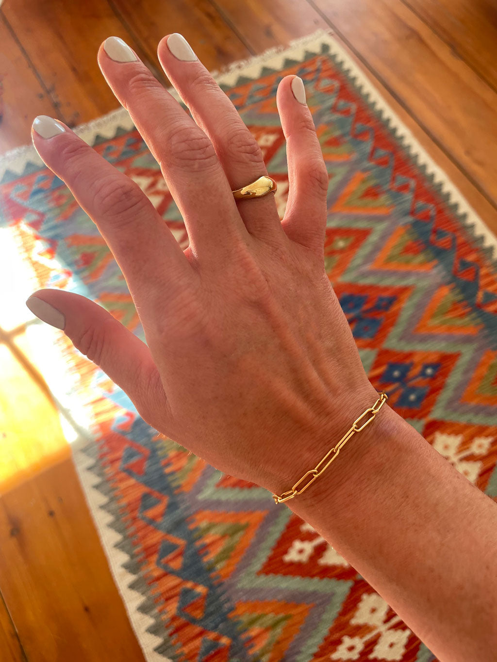 hand against colorful rug with chunky gold ring and thick gold chain bracelet