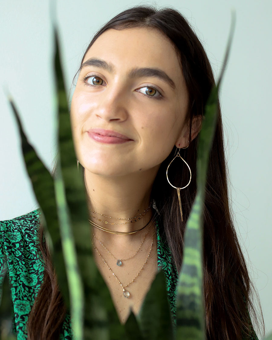 brunette girl behind a plant wearing 14k gold filled teardrop fringe earrings