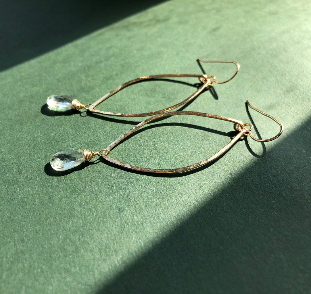 14k gold filled green amethyst leaf gemstone earrings on a green surface under direct sunlight