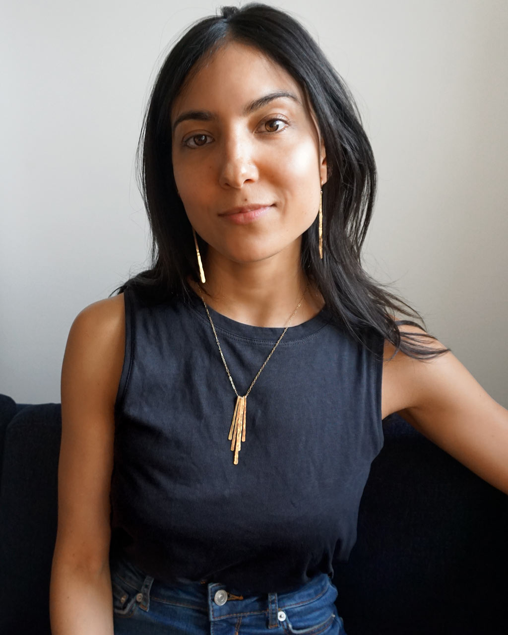 brunette wearing navy blue top facing camera wearing a 14k gold filled xl single stroke fringe earrings and rays pendant