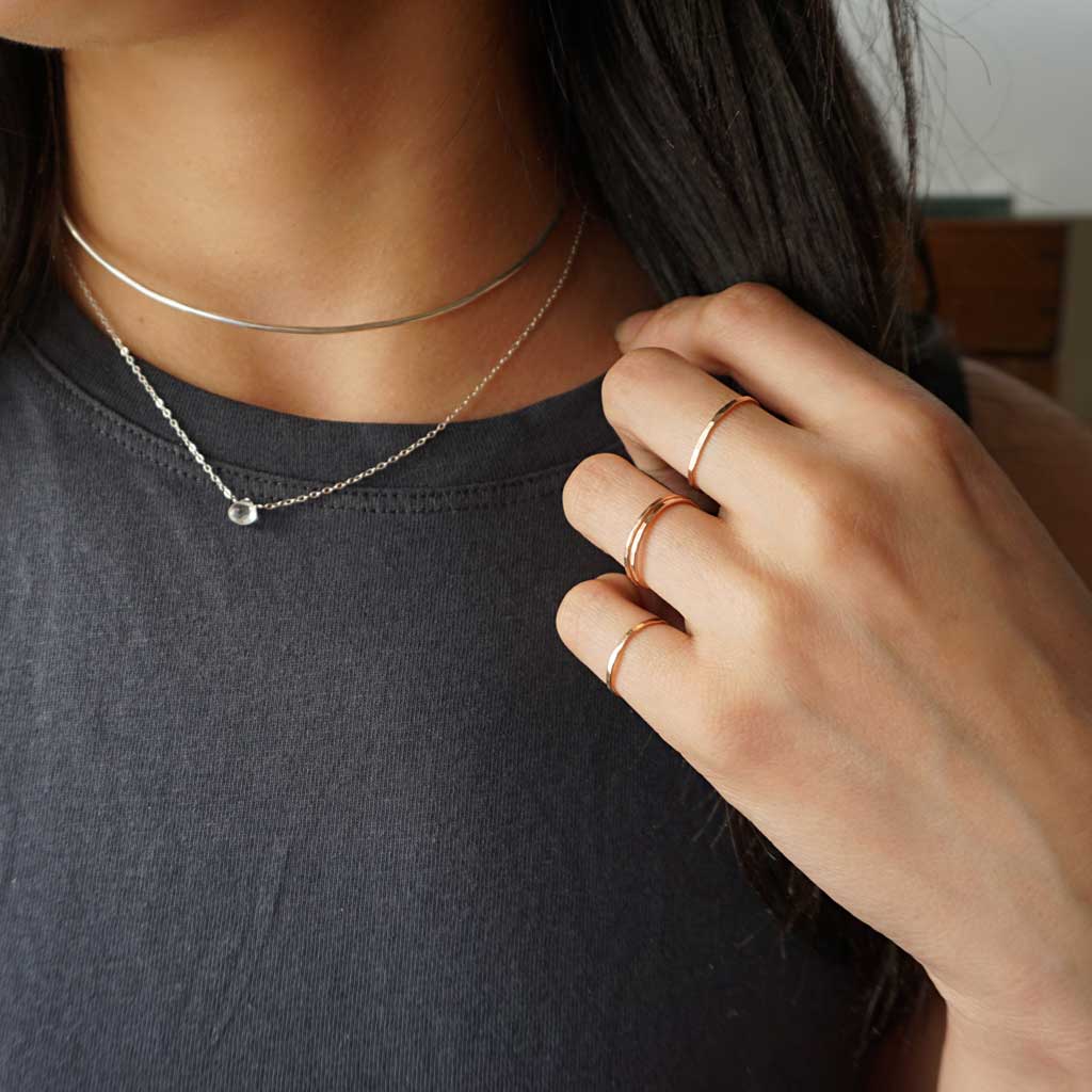 woman neck close-up wearing white topaz short gemstone necklace sterling silver halo collar and thin rose gold stacking rings