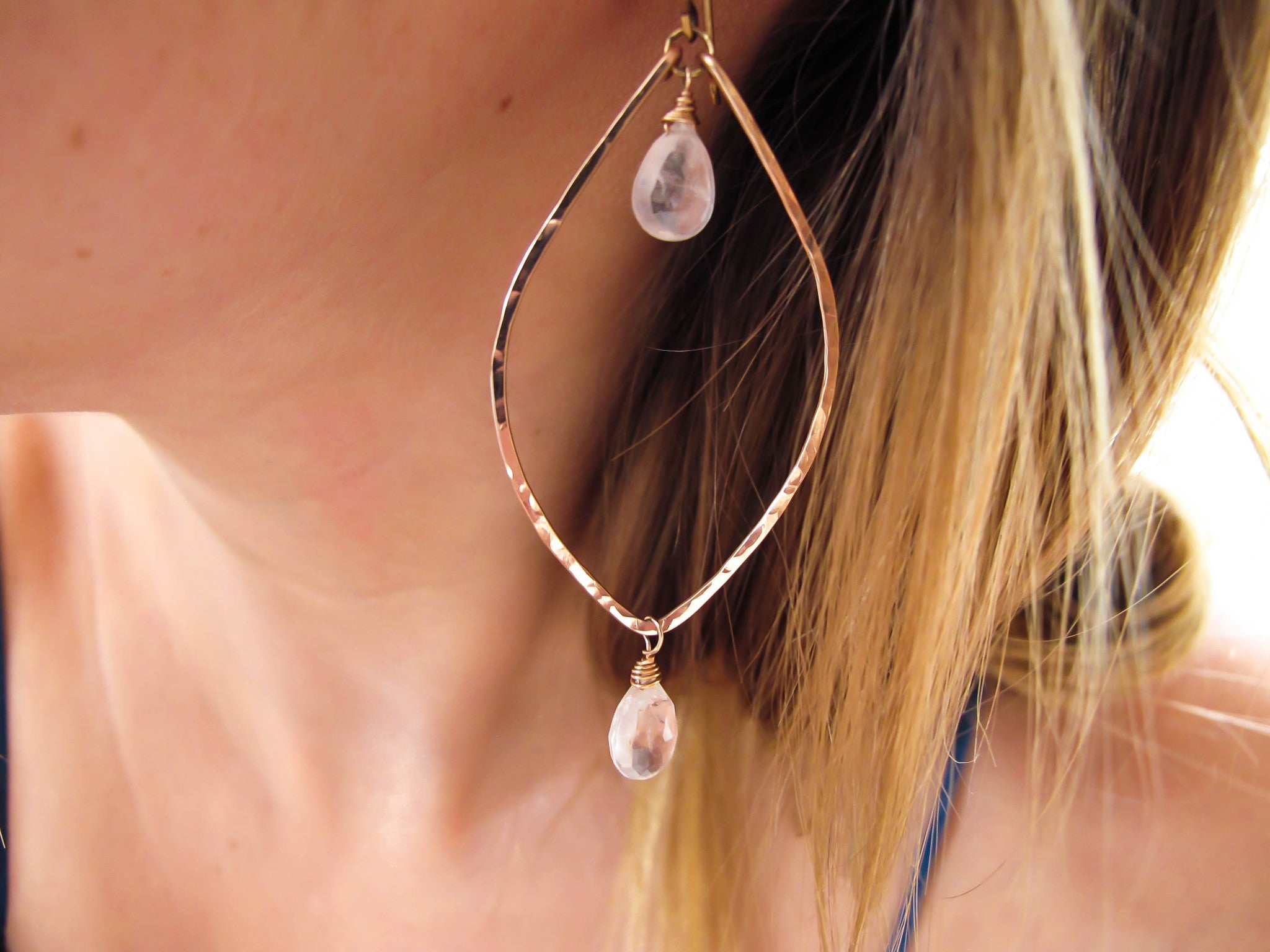 blond woman on a blue top ear closeup wearing rose quartz rose gold leaf gemstone earrings partially reflecting light