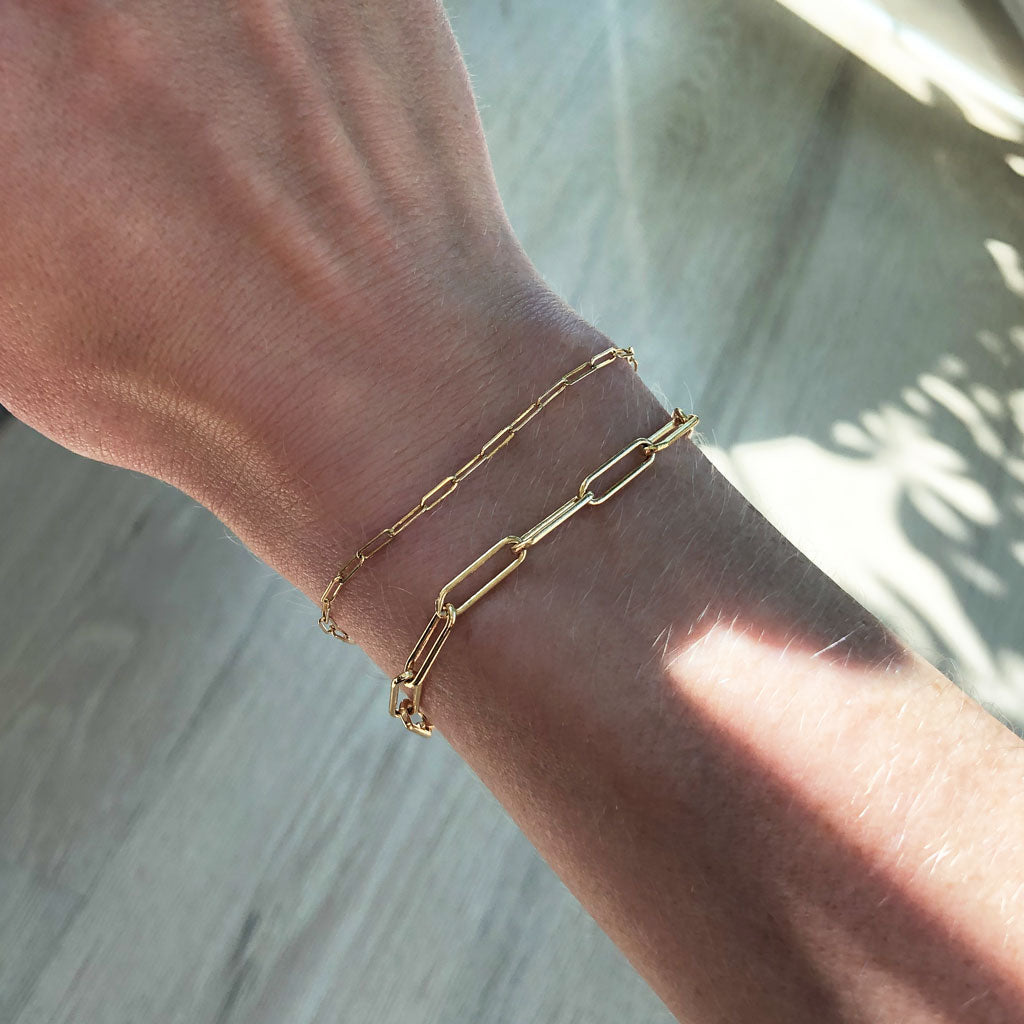 woman wrist wearing 14k gold filled small link and large link chain bracelets against wood floor