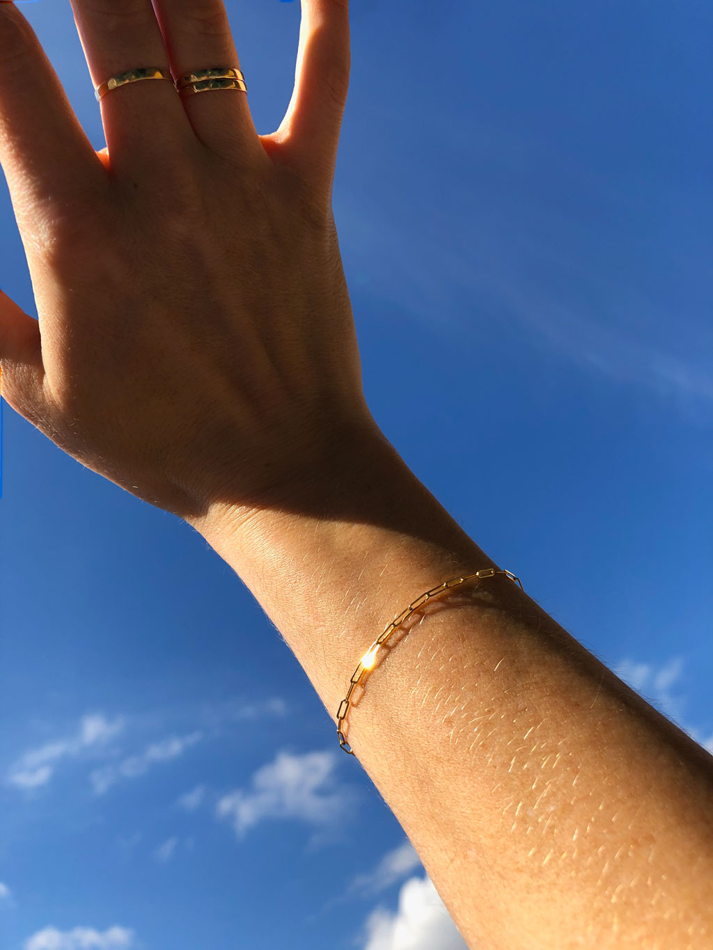 woman hand wearing thin gold stacking rings on middle and ring fingers and a 14k gold filled small link chain bracelet