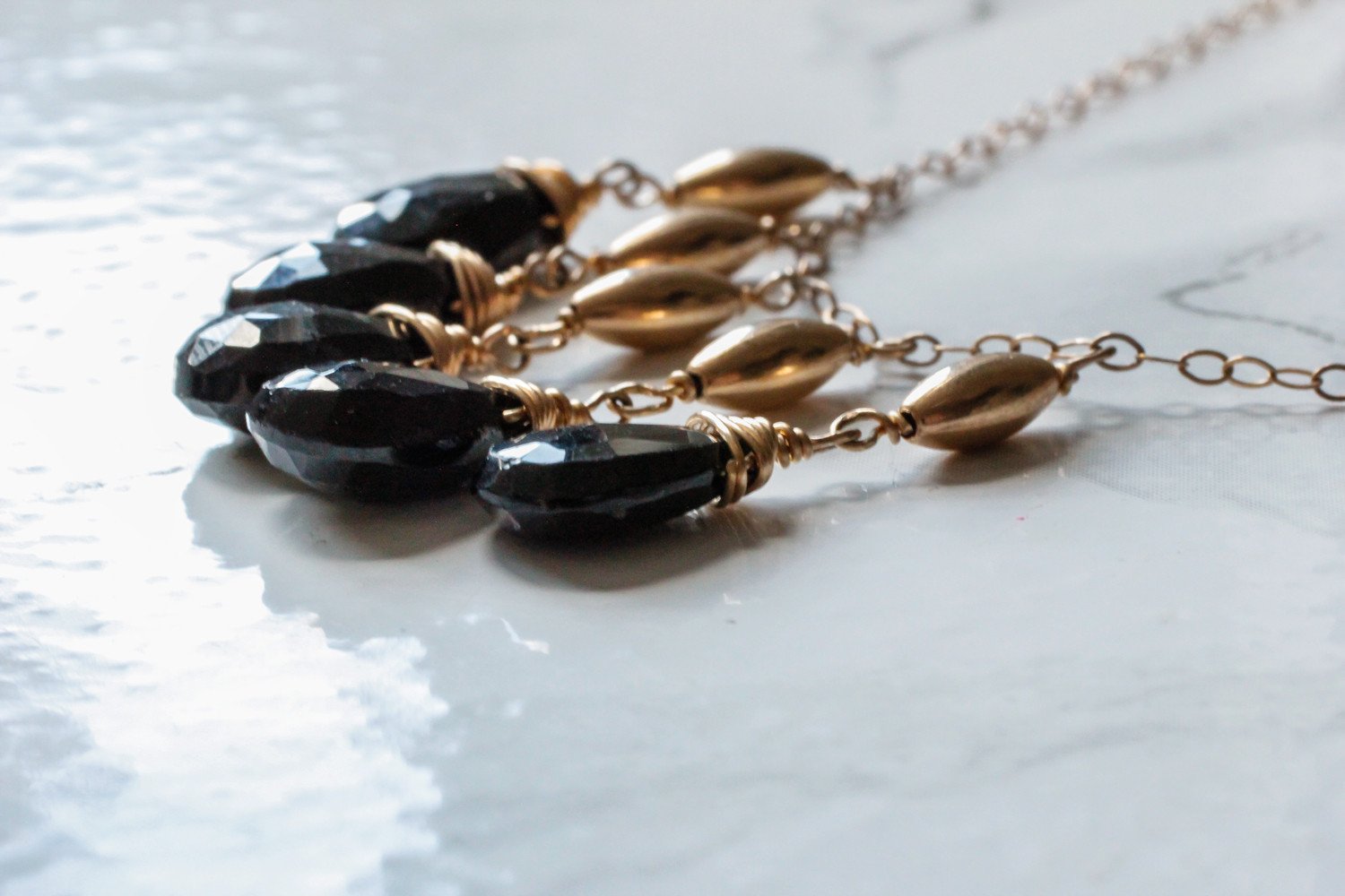 high closeup of a black spinel stone from a 14k gold filled black spinel cascade gemstone necklace on a shiny white surface