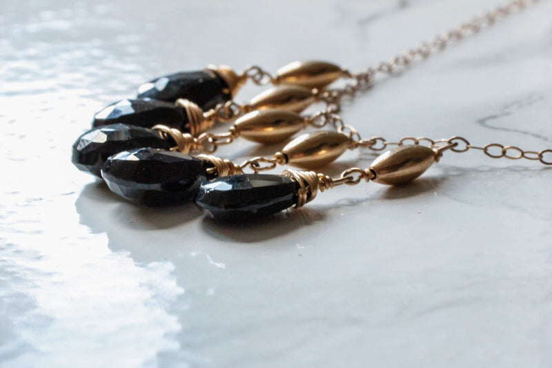 high closeup of a black spinel stone from a 14k gold filled black spinel cascade gemstone necklace on a shiny white surface 