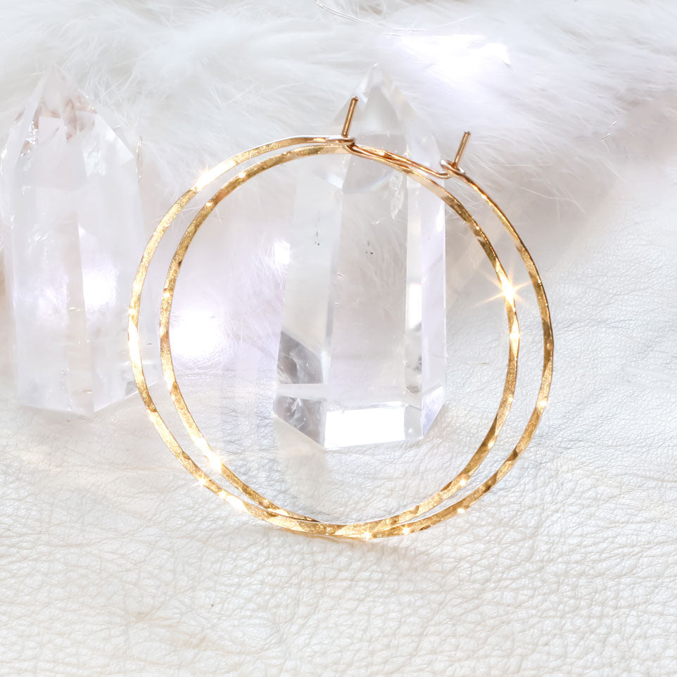 14k gold filled 2 inch endless thin hoop earrings laying on crystal quartz under a shiny bright light on white surface