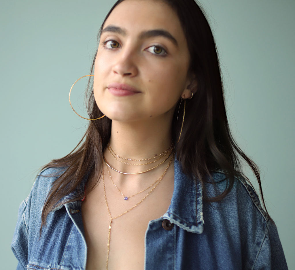 girl with layered delicate gold choker, tanzanite necklace and large hoops